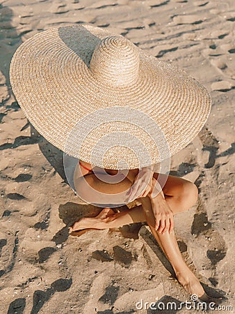 Young attractive woman in bikini with big straw hat posing at sandy beach Stock Photo