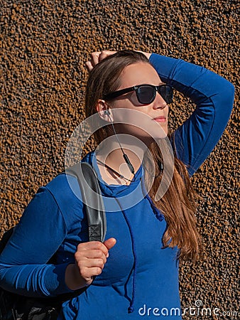Young attractive woman in blue hoody black sunglasses on wall background listening to music with Wi-Fi headphones Stock Photo