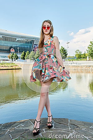 Young attractive woman. Red sunglasses, color dress. Girl`s portrait. Football stadium background. Stock Photo