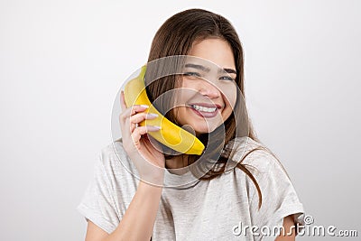 Young attractive woman holding banana like a phone in her hand looking happy standing on isolated white background dietology and Stock Photo