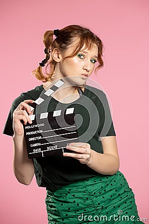 Young attractive woman holding film clapper. Teen girl in a blue shirt and glasses holding classic black film making Stock Photo