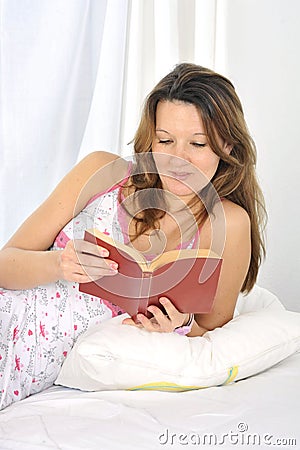 Young attractive woman in nightgown lying relaxed on bed reading novel book Stock Photo