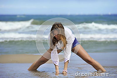 Young attractive woman in shorts and shirt playing with sand on the beach with sea on her back Stock Photo