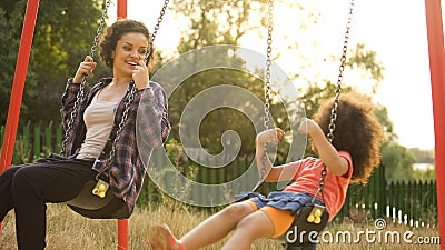 Young babysitter playing with carefree kid, swinging outdoor at child playground Stock Photo