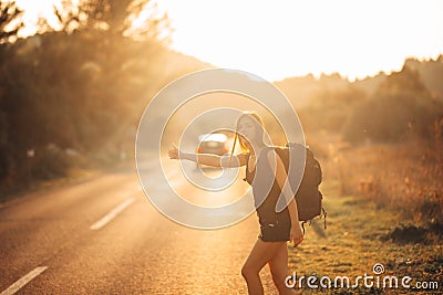 Young backpacking adventurous woman hitchhiking on the road. Stopping a car with a thumb. Travel lifestyle. Low budget traveling Stock Photo