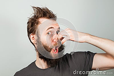 Young baerded guy close nose from a bad smell on gray background Stock Photo