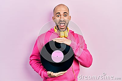 Young bald man holding vinyl disc celebrating crazy and amazed for success with open eyes screaming excited Stock Photo