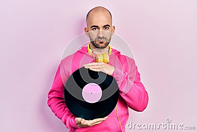 Young bald man holding vinyl disc relaxed with serious expression on face Stock Photo