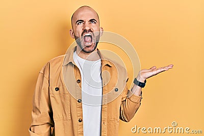 Young bald man presenting with open palms, holding something angry and mad screaming frustrated and furious, shouting with anger Stock Photo