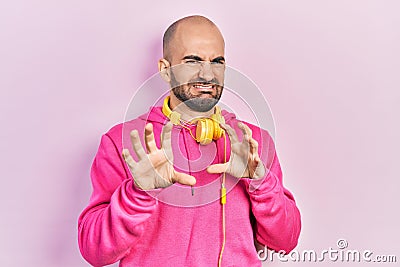 Young bald man wearing gym clothes and using headphones disgusted expression, displeased and fearful doing disgust face because Stock Photo
