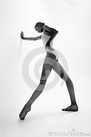 young ballerina in a bodysuit is leaning with her hand on the wall and taking a step with her foot Stock Photo