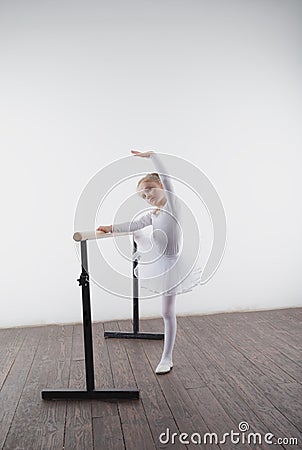 Young ballerina girl in a white tutu. Adorable child dancing classical ballet in a white studio with wooden floor. Children dance. Stock Photo