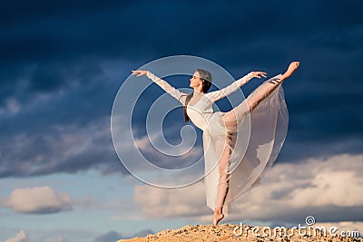 Young ballerina in a light long white dress stands in an arabesque Stock Photo