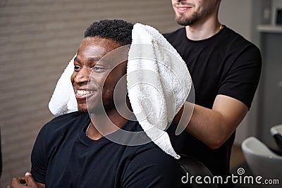 Young barber dries clients hair with soft towel Stock Photo