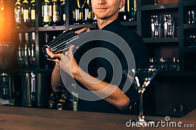 Young barman in bar interior shaking and mixing alcohol cocktail. Professional bartender portrait at work in night club Stock Photo