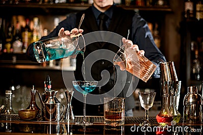 Young bartender professionally pours cocktails into glasses. Stock Photo