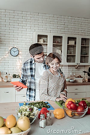 Young beaming pretty woman with big earrings and her husband cutting greens together Stock Photo