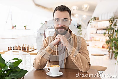 Young bearded attractive man drinks coffee during his lunch break in the cafe, positive vibes Stock Photo