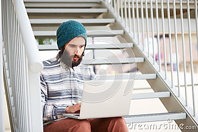 Young bearded hipster student using computer outdoors Stock Photo