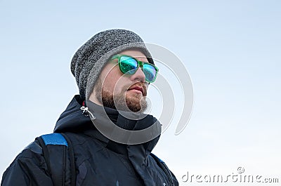 Young bearded hipster wearing a hat and sunglasses with Nordic walking sticks and a backpack moves in the mountains at Stock Photo