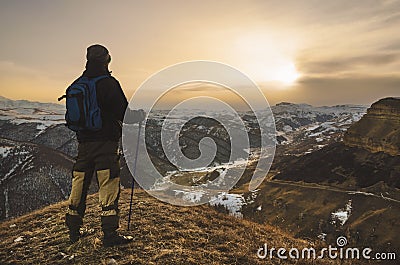 Young bearded hipster wearing a hat and sunglasses with Nordic walking sticks and a backpack moves in the mountains at Stock Photo