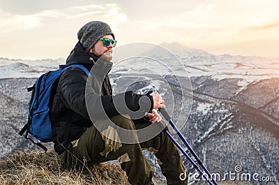 Young bearded hipster wearing a hat and sunglasses with Nordic walking sticks and a backpack moves in the mountains at Stock Photo