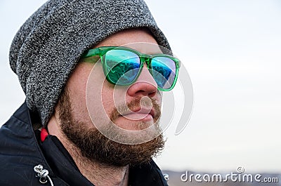 Young bearded hipster wearing a hat and sunglasses with Nordic walking sticks and a backpack moves in the mountains at Stock Photo