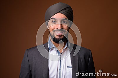 Young bearded Indian Sikh businessman wearing turban against bro Stock Photo