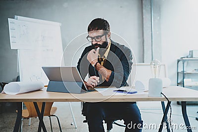 Young bearded male architect wearing eye glasses working on a digital tablet dock at his desk. Professional experienced Stock Photo