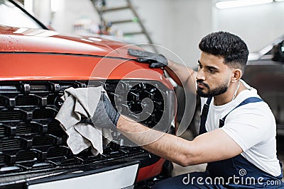 Young bearded male professional car wash worker, holding the gray microfiber and wiping grille Stock Photo