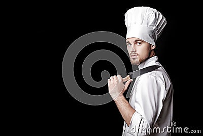 Young bearded man chef In white uniform holds knife on black background Stock Photo