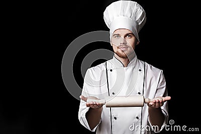 Young bearded man chef In white uniform holds rolling pin on black background Stock Photo