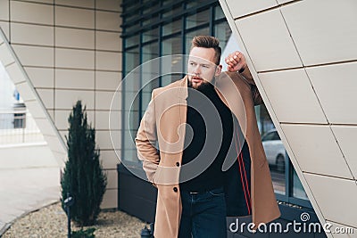 Young bearded man with modern hairstyle and trendy coat standing near business center Stock Photo