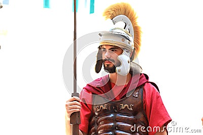 A young bearded man in a red uniform of a Roman legionary, in a metal helmet, tunic and with a spear stands in Editorial Stock Photo