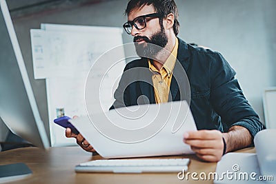 Young bearded man working at sunny while sitting at wooden table.Designer analyze new ideas on modern computer.Blurred Stock Photo