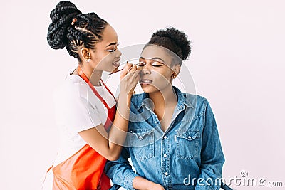 Young beautiful African American woman applying professional make-up by African make-up artist. Studio shoot Stock Photo