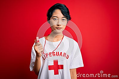 Young beautiful asian lifeguard girl wearing t-shirt with red cross using whistle Relaxed with serious expression on face Editorial Stock Photo