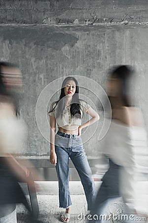 Young beautiful Asian woman standing casually posing for the camera at an indoor rustic place while people walking blurry in front Stock Photo