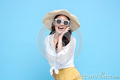 Young beautiful Asian woman in summer casual clothes wearing straw hat, sunglasses say something and hand side mouth and smile on Stock Photo