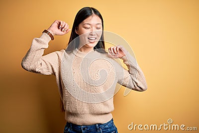 Young beautiful asian woman wearing casual sweater over yellow isolated background Dancing happy and cheerful, smiling moving Editorial Stock Photo