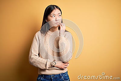 Young beautiful asian woman wearing casual sweater over yellow isolated background with hand on chin thinking about question, Editorial Stock Photo