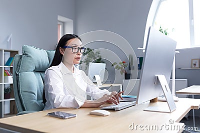 A young beautiful Asian woman is working at a computer in the office. Businesswoman at the desk Stock Photo