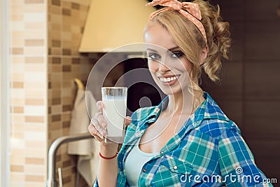 Young beautiful blond housewife in the kitchen holding a glass of milk and smiling Stock Photo