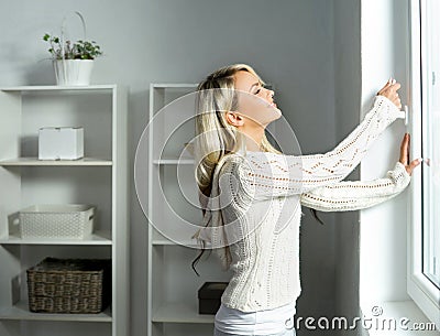 Young and beautiful blond woman opening the window Stock Photo