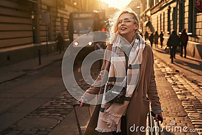 Young beautiful blond woman tourist with a wheeled travel bag and vintage film camera arrives to a new city on a sunny Stock Photo