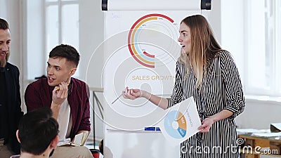 Young beautiful blonde business woman coach leading team discussion, presenting project at modern office flipchart. Stock Photo