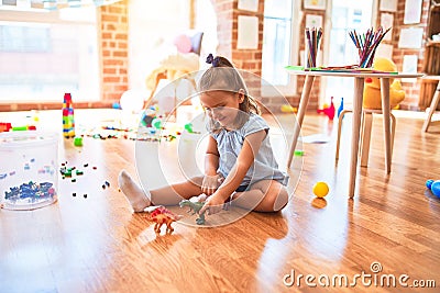 Young beautiful blonde girl kid enjoying play school with toys at kindergarten, smiling happy playing with dinosaurs toys at home Stock Photo