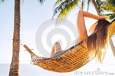 Young beautiful blonde longhaired woman relaxing in hammock under palm trees on the sand beach Stock Photo