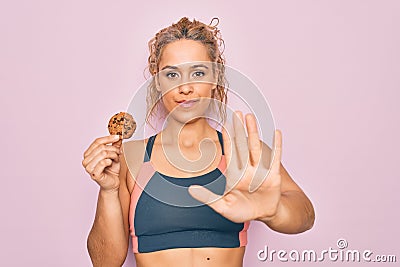 Young beautiful blonde sporty woman doing sport holding cookie over isolated pink background with open hand doing stop sign with Stock Photo