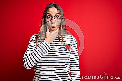 Young beautiful blonde woman with blue eyes wearing glasses standing over red background Looking fascinated with disbelief, Stock Photo
